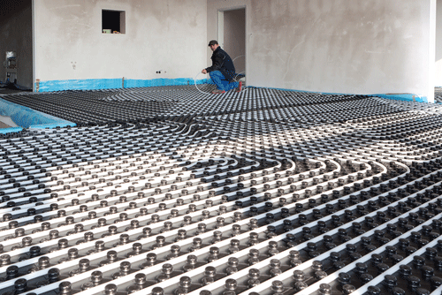 Radiant floor A technician installs a radiant floor heating system in a large room, carefully arranging heated water tubing over the insulated base layer.