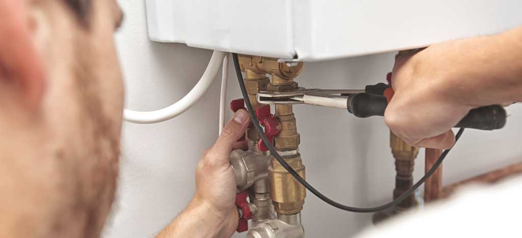 Close up of plumber using wrench to tighten copper pipe under sink