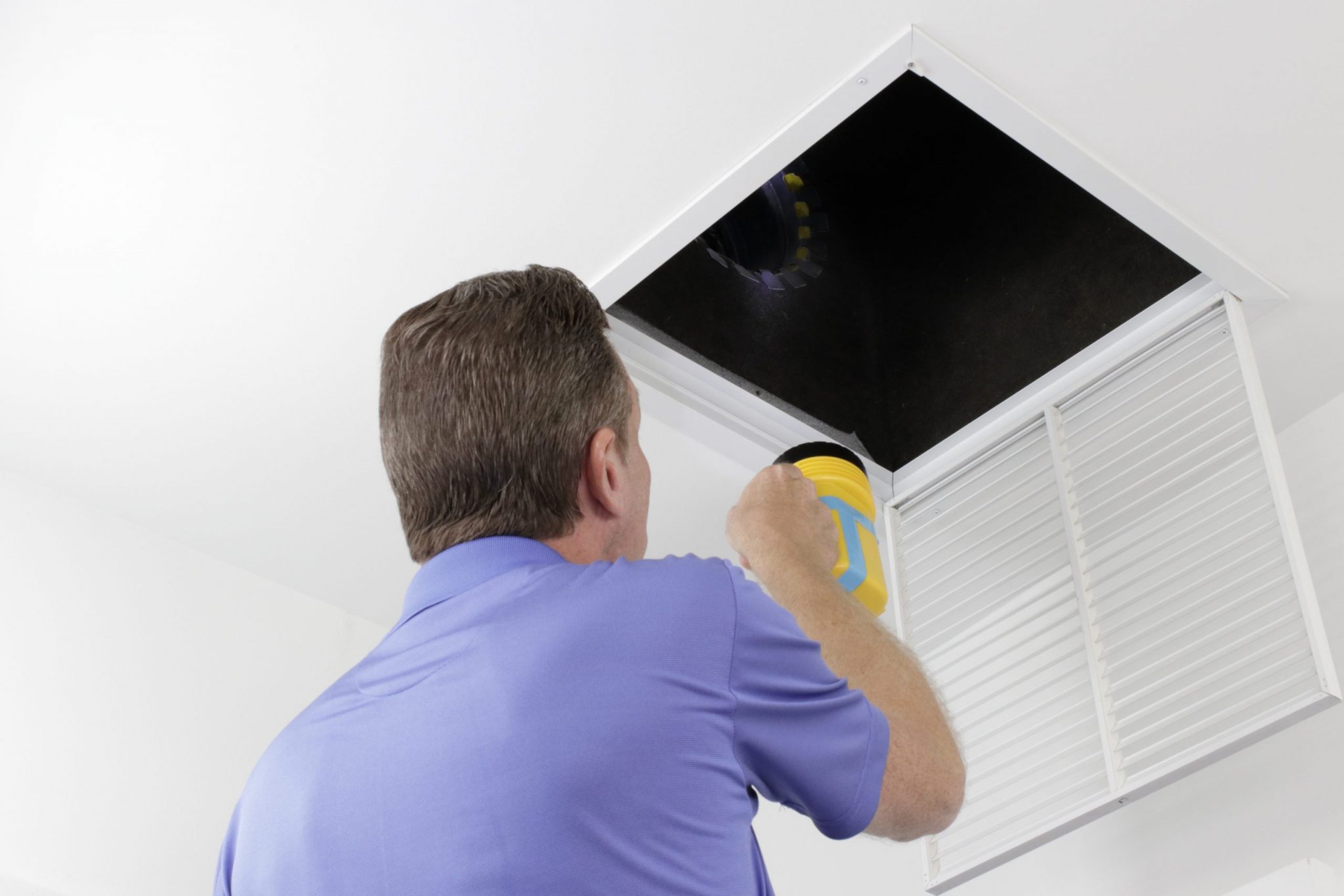 Older male with a yellow flashlight examining HVAC ducts in a large square vent.