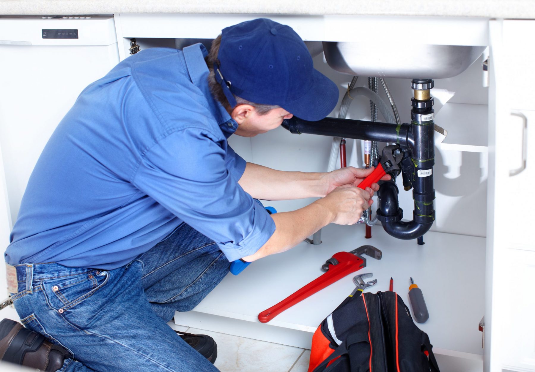 Older plumber fixing a sink at kitchen
