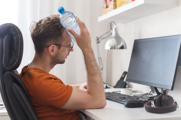 Man at computer in summer time with water bottle to head