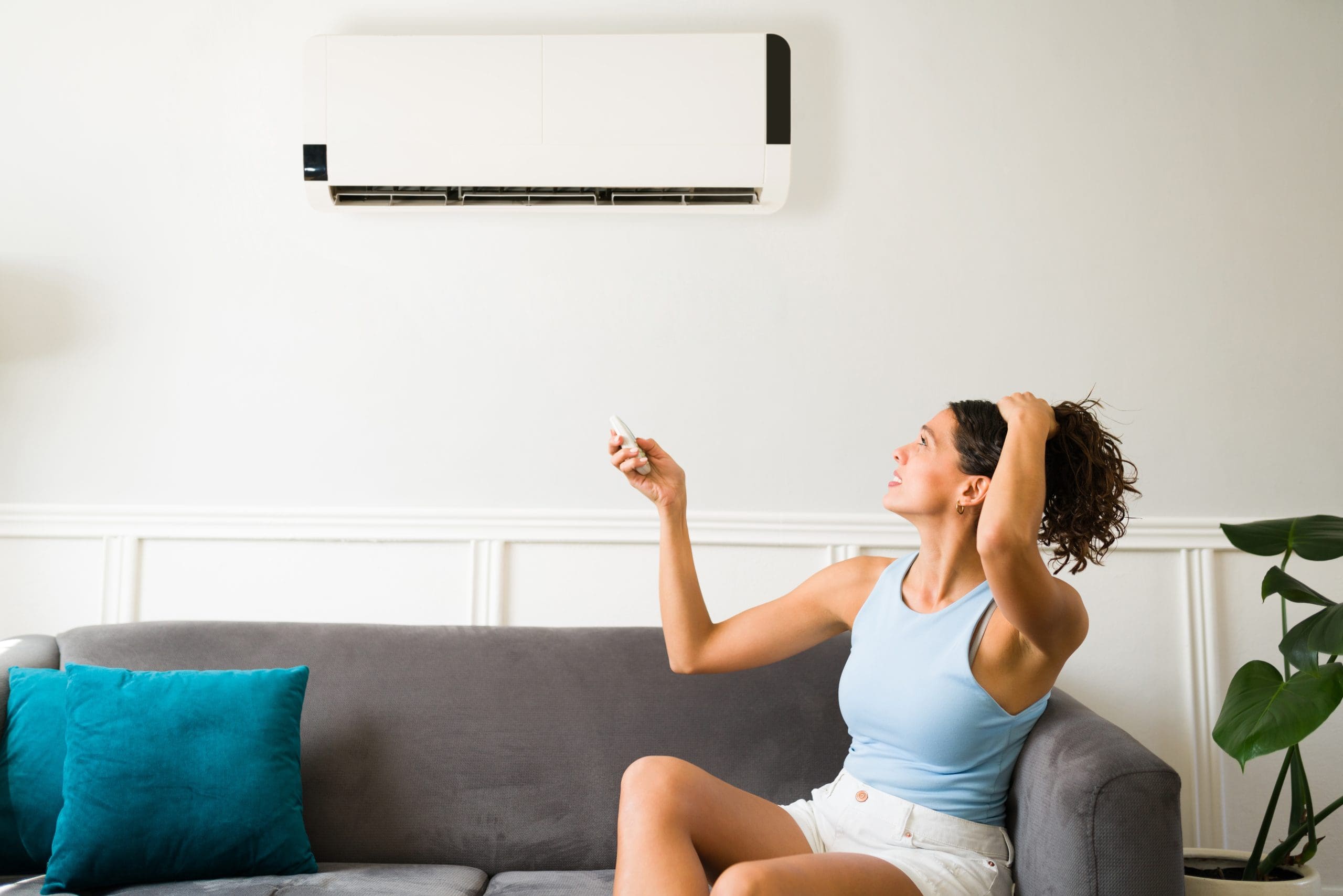 Young woman looking uncomfortable and pointing remote at AC unit on wall