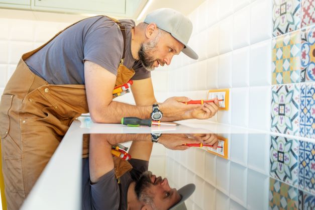 Electrician reaching over counter to address electrical socket