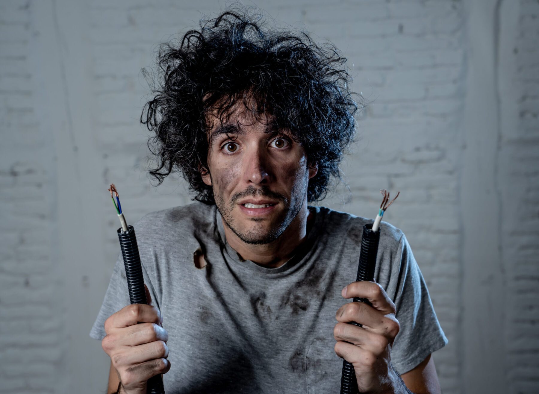 Man holding two wire ends looking like he was electrocuted.