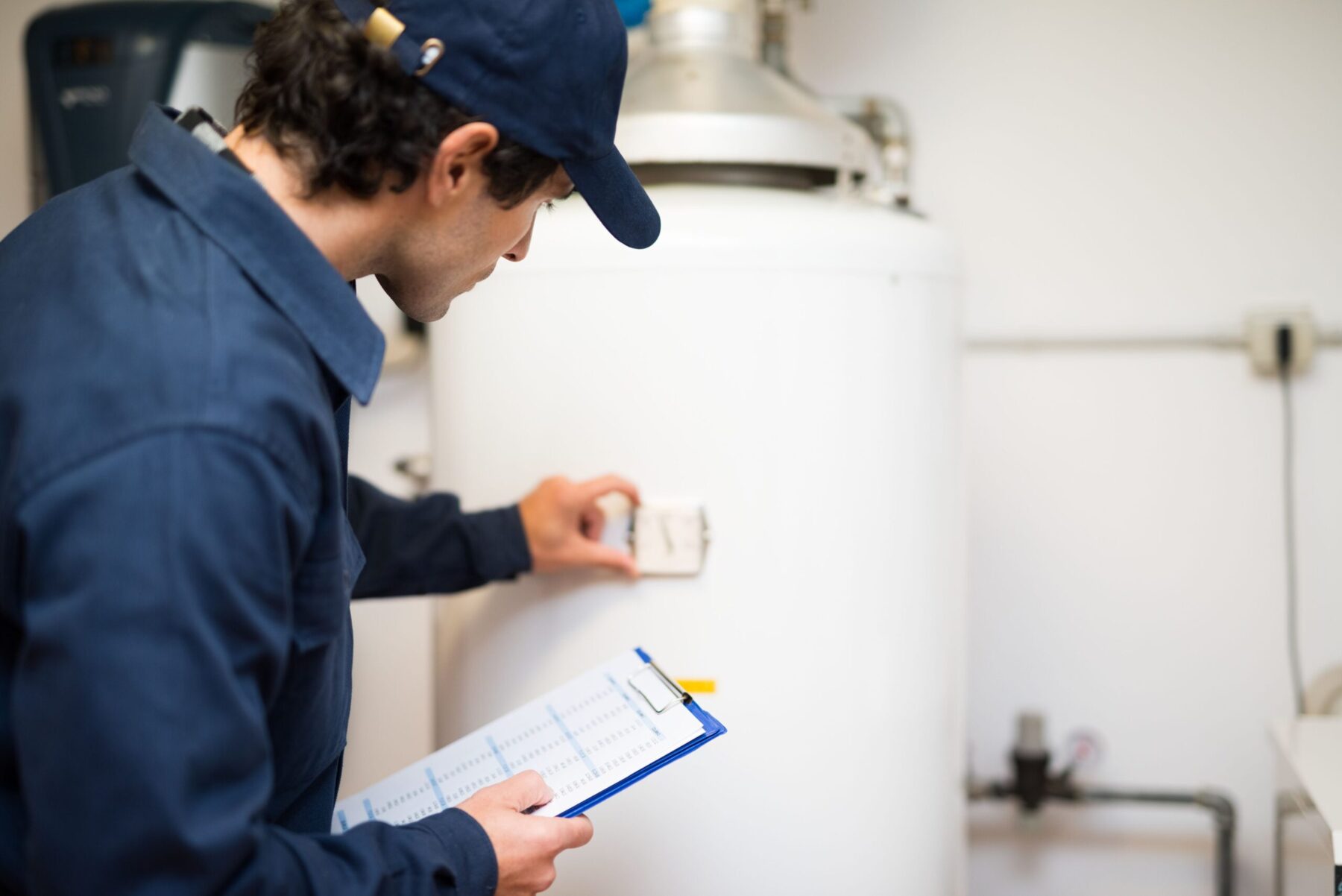 Plumber checking the side of a hot water tank holding clipboard
