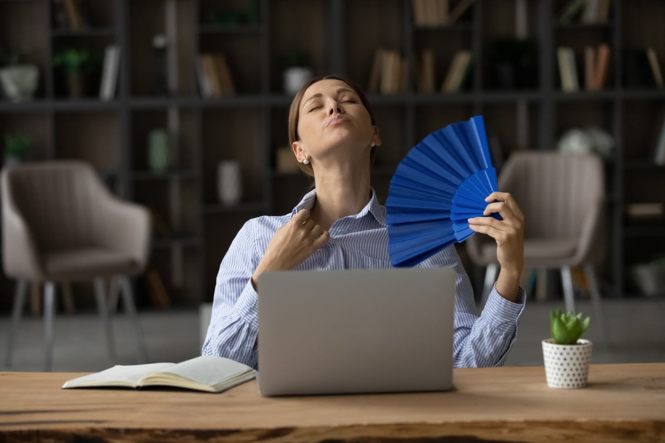 Woman sitting at a desk and fanning herself with a blue paper fan