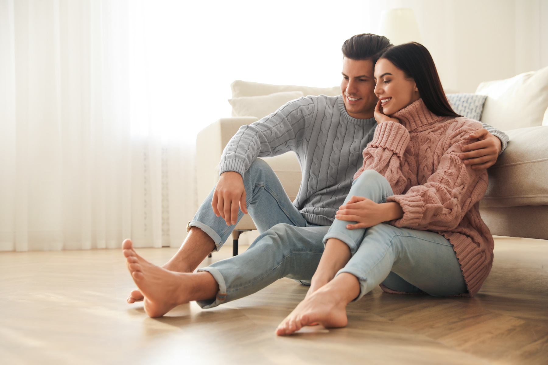 Happy couple sitting on warm floor in living room. Heating system.