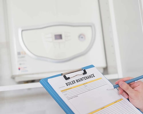 Boiler maintenance Technician holding a clipboard labeled “Boiler Maintenance” near a wall-mounted boiler.