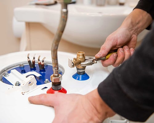 Person tightening a valve on top of a water heater using pliers.