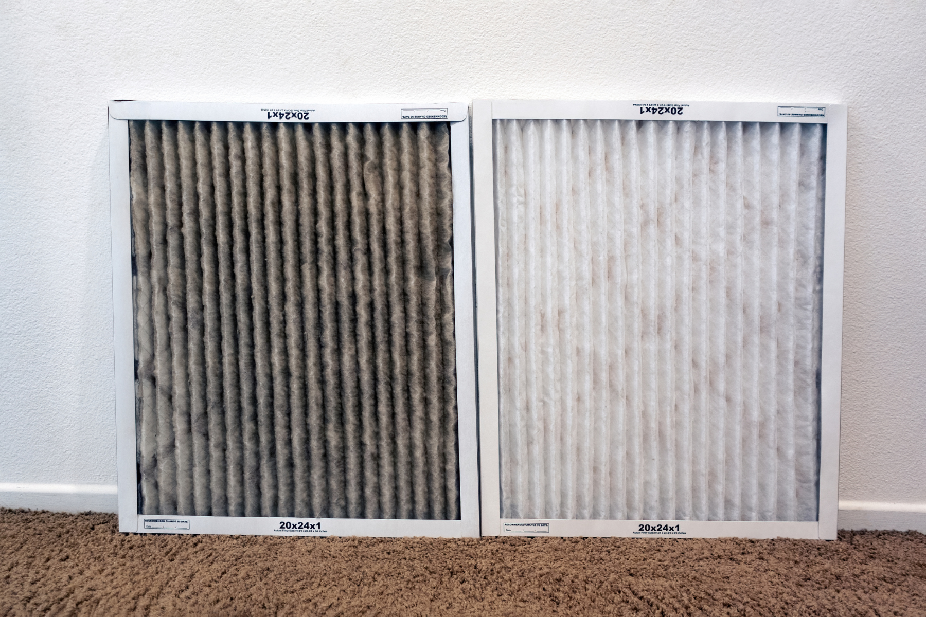 Comparison of a dirty air filter on the left and a clean air filter on the right, placed against a white wall and beige carpet background
