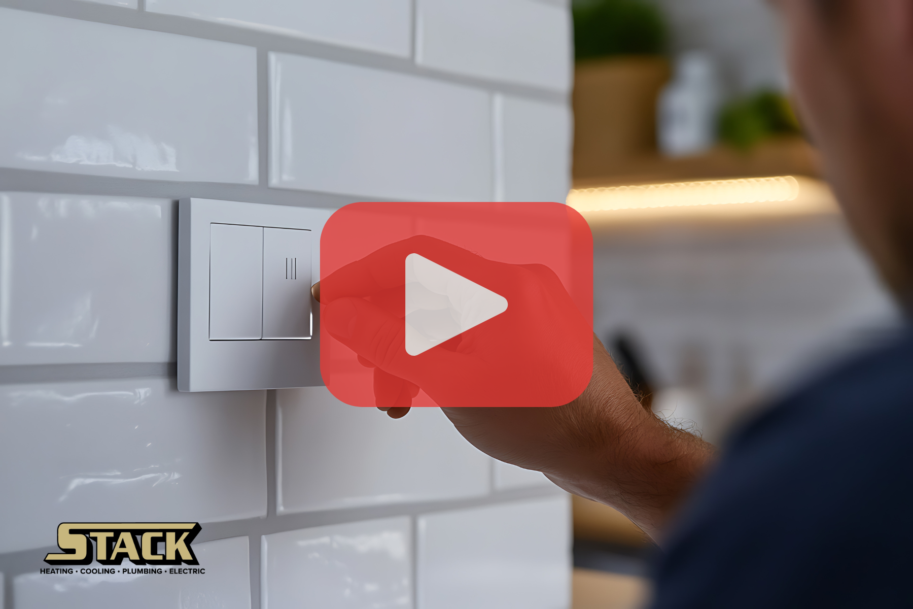 A close-up of a person’s hand turning on a sleek light switch on a tiled kitchen wall, with a Stack logo and video icon overlay.