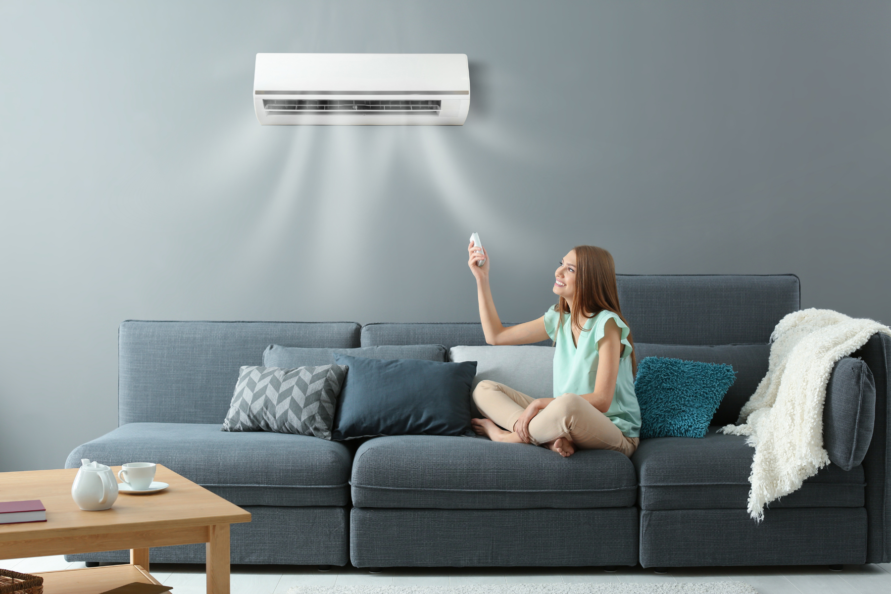 Young woman happily adjusting a modern AC unit while relaxing on a couch.