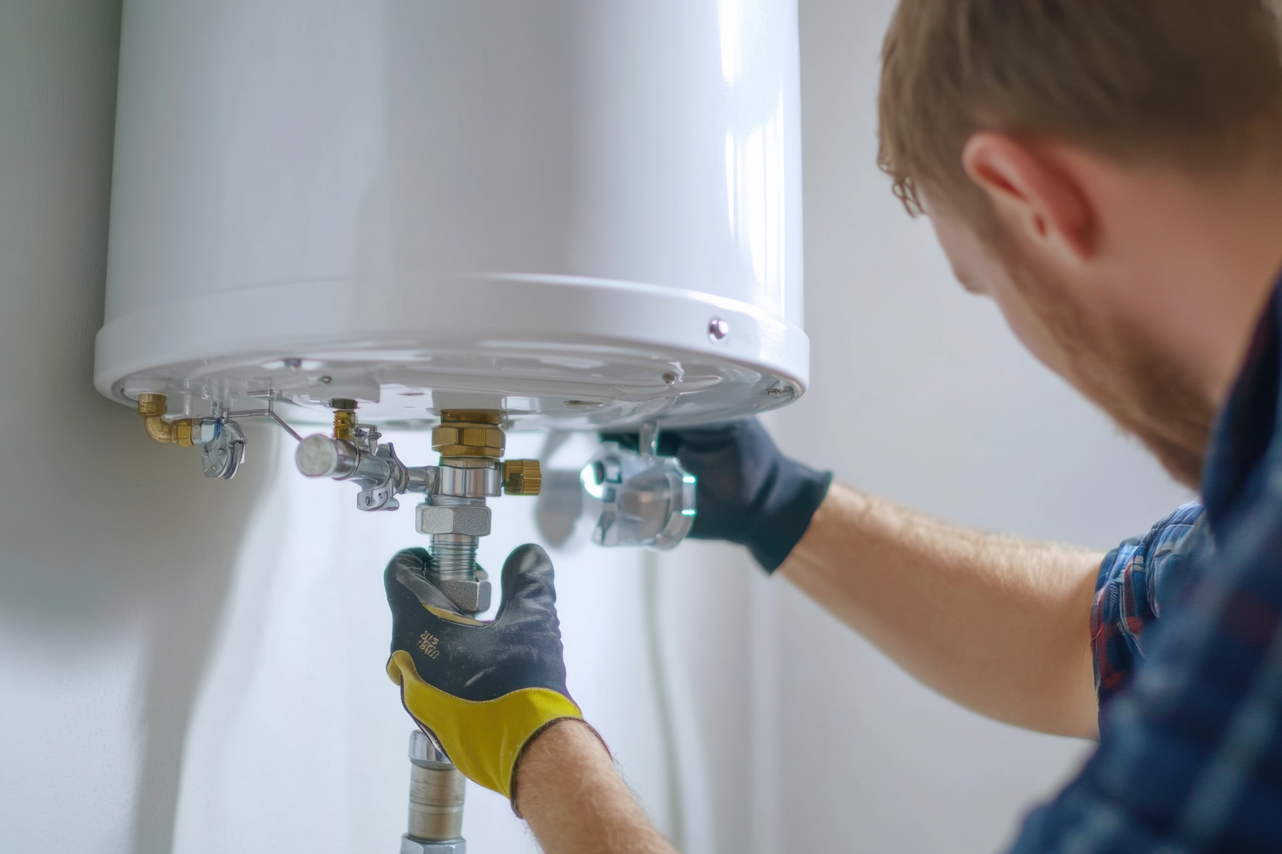 Water heater maintenance A close-up of a technician adjusting connections beneath a mounted water heater, wearing protective gloves.