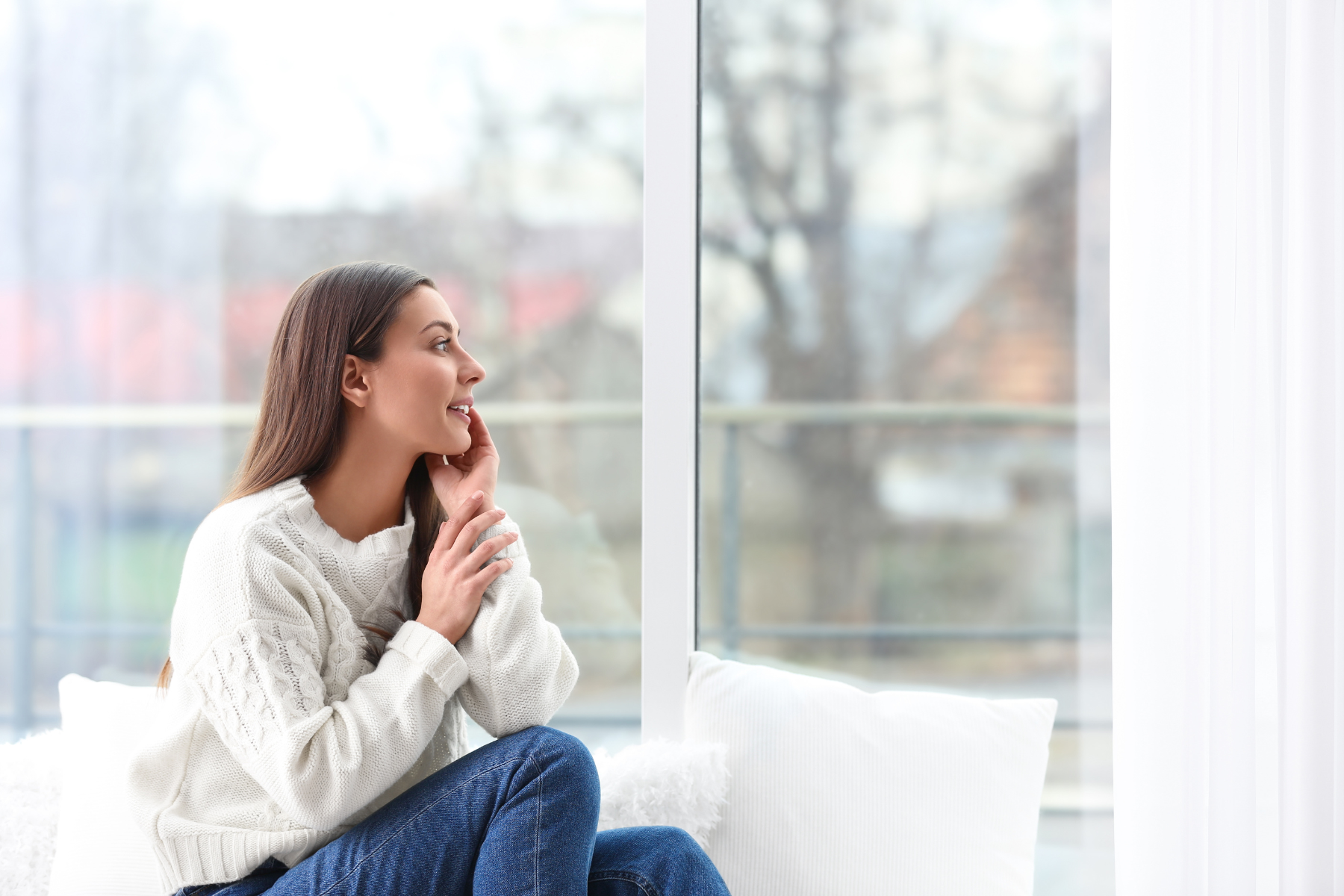 A cheerful woman sits warmly dressed inside her home.