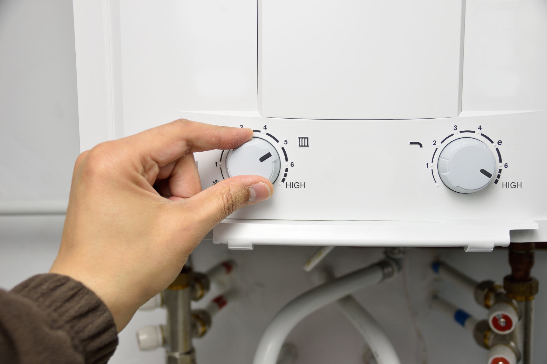 A hand is adjusting the temperature dial on a water heater unit.