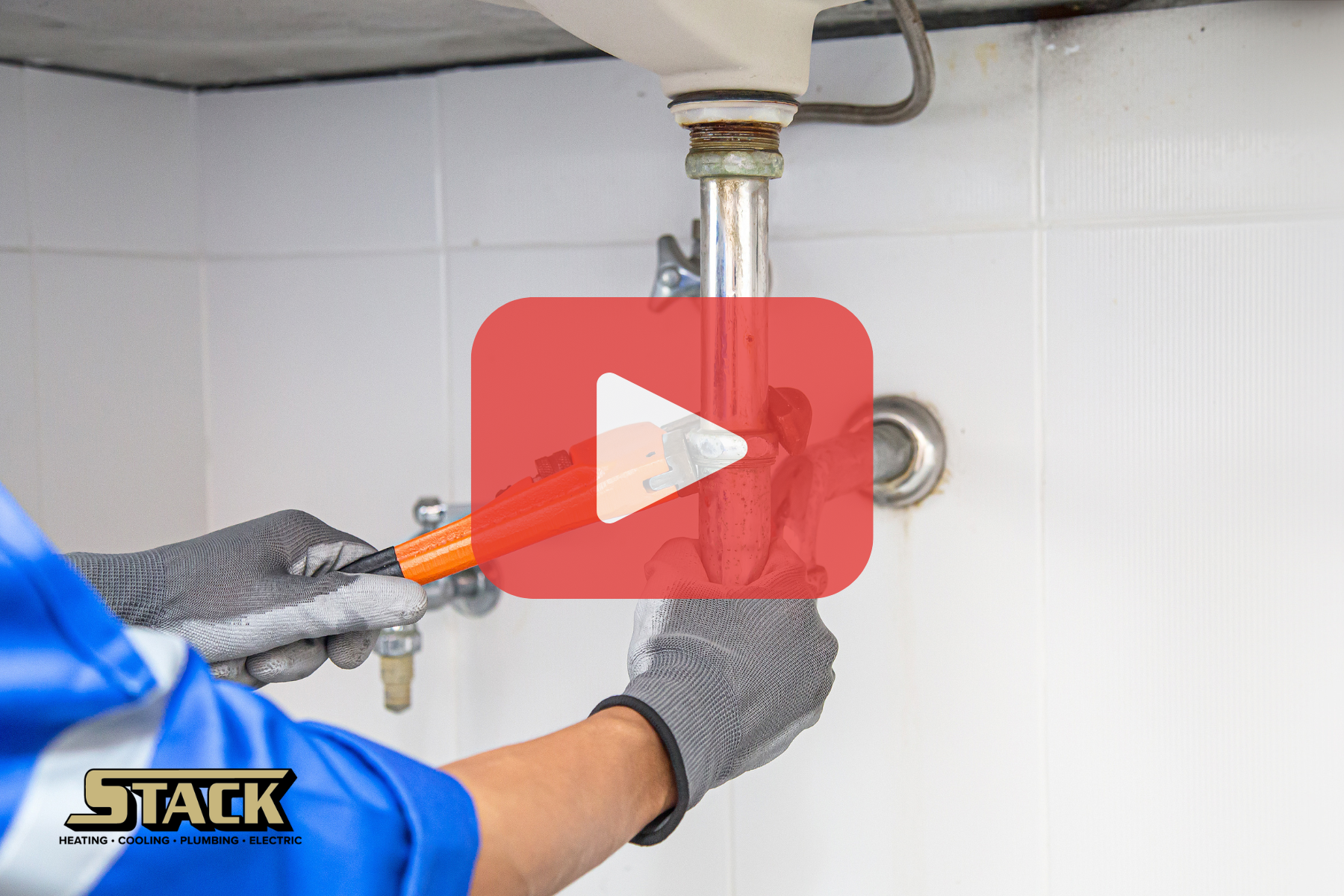 A plumber using a wrench to work on a pipe under a sink.