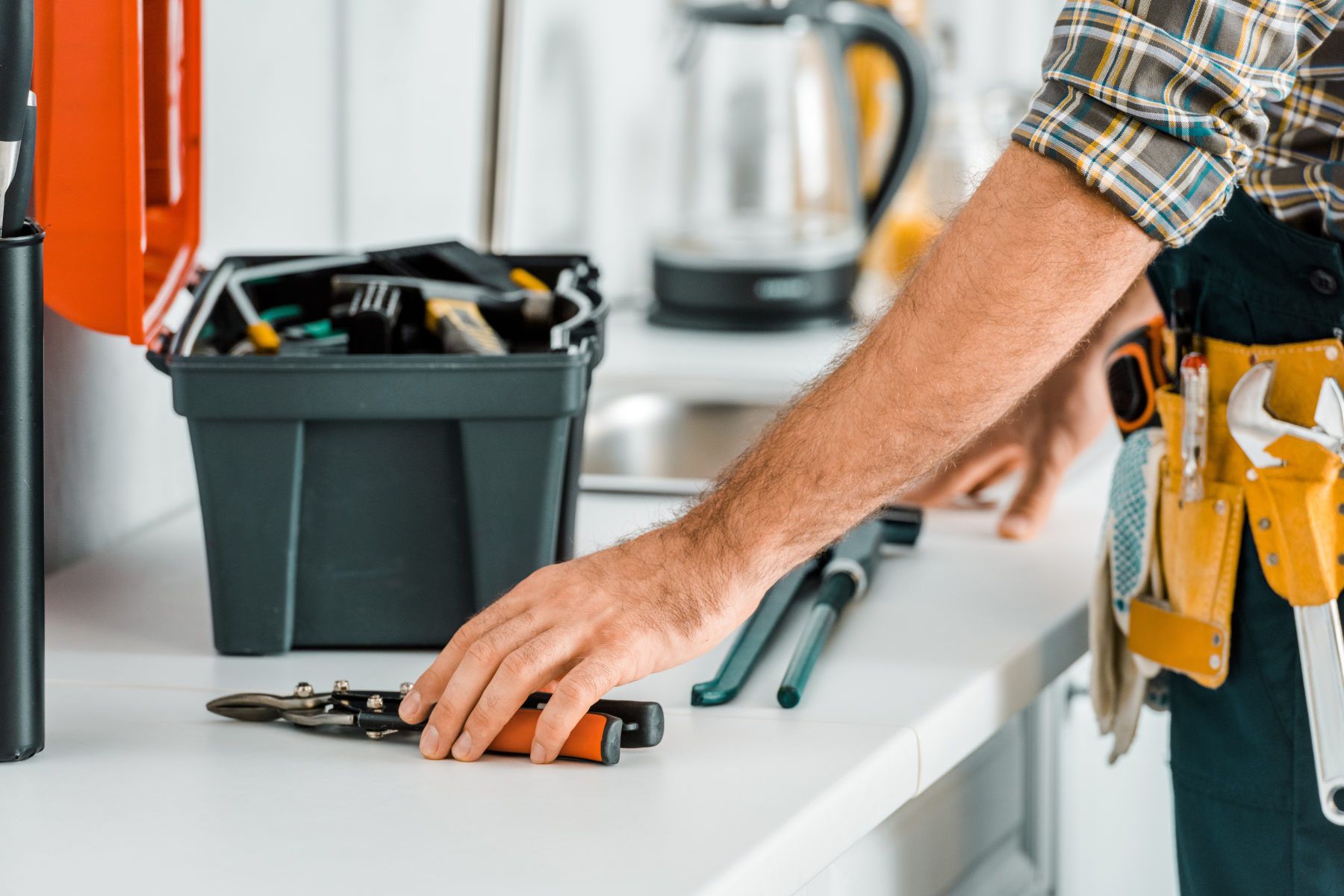A plumber reaching for tools on a countertop with a toolbox and equipment nearby.