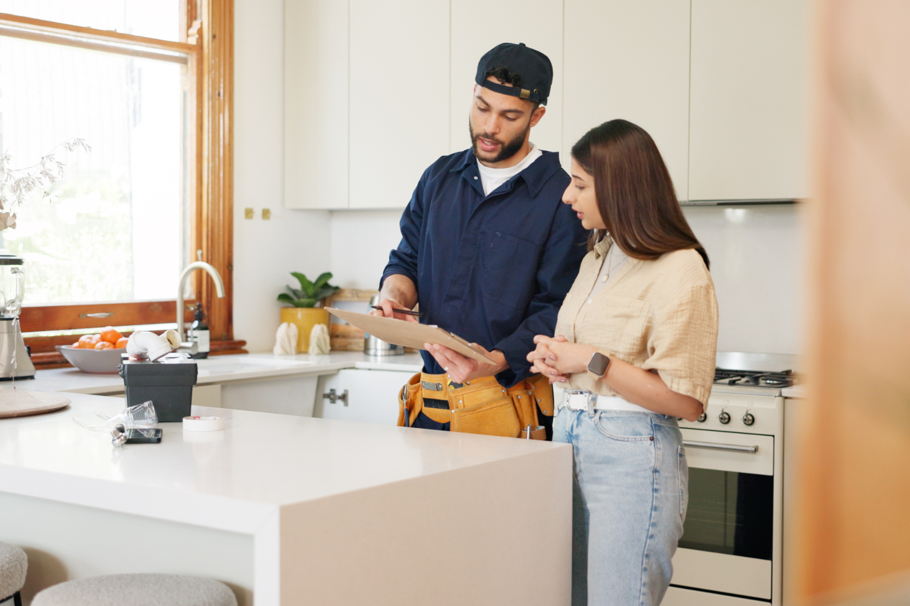 A plumber explaining details on a clipboard to a woman in a kitchen.