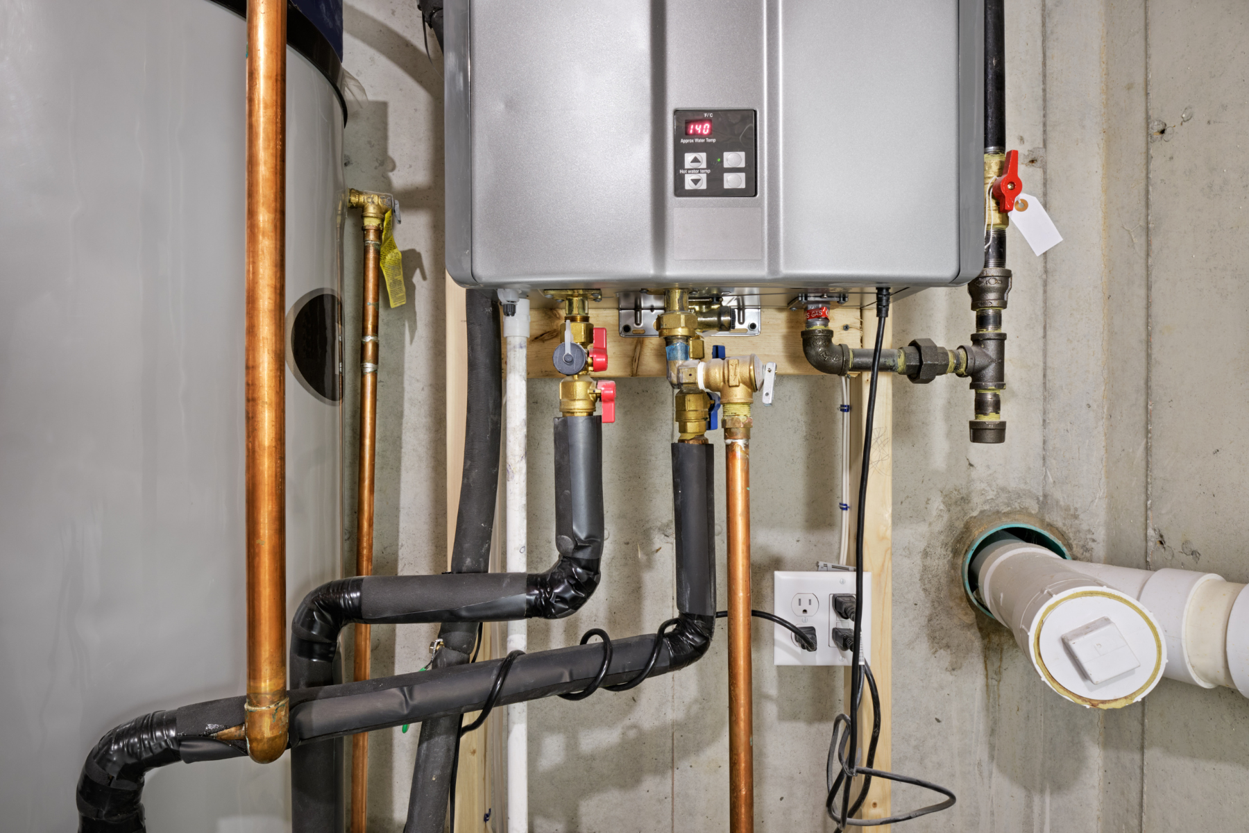 A residential boiler room with a tankless water heater and connected copper pipes.