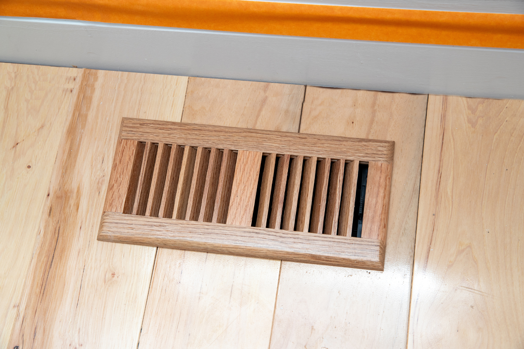A natural wood floor register blending into hardwood flooring, showing a home heating vent.