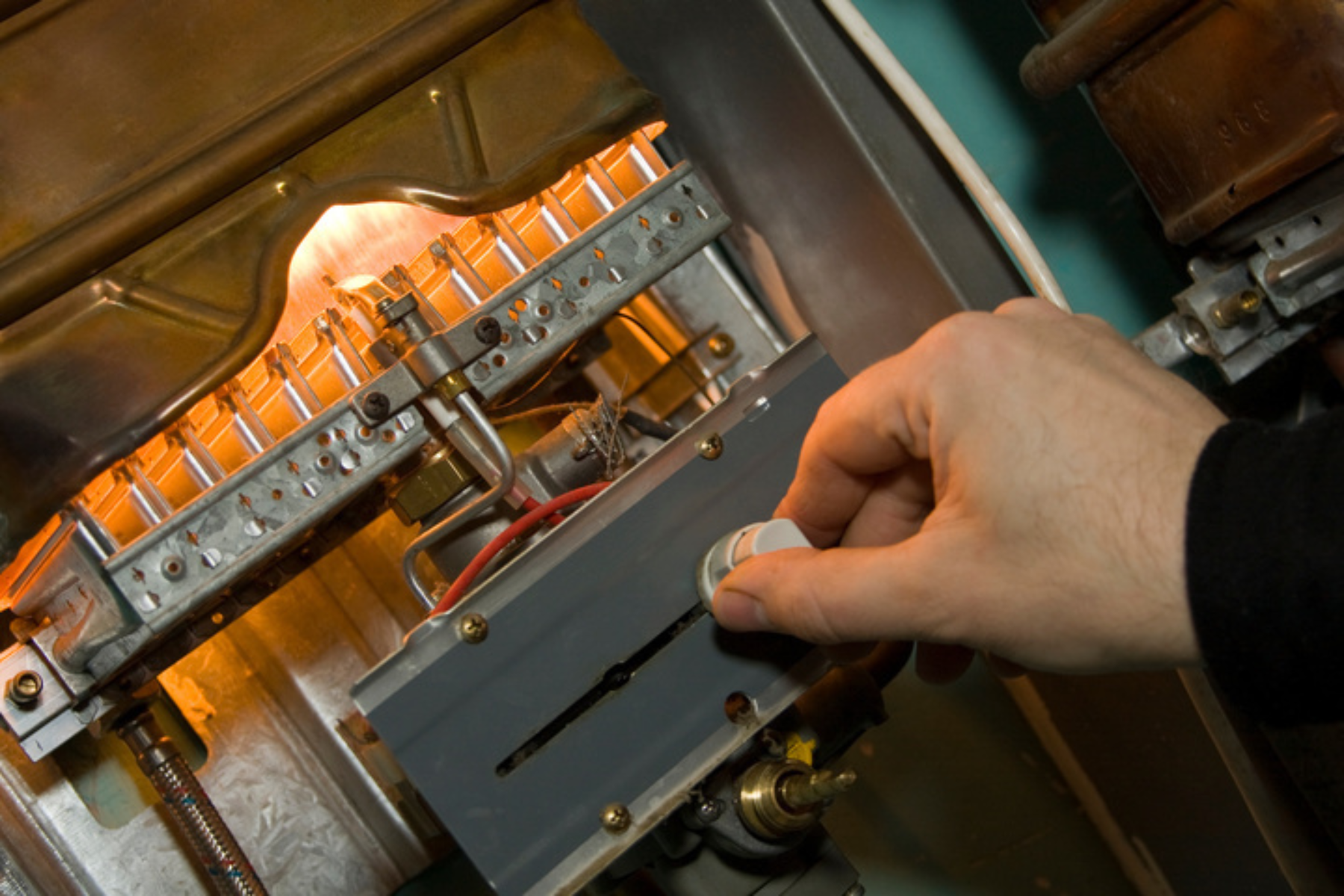 A person’s hand turning a control knob on a gas furnace with burners lit inside.