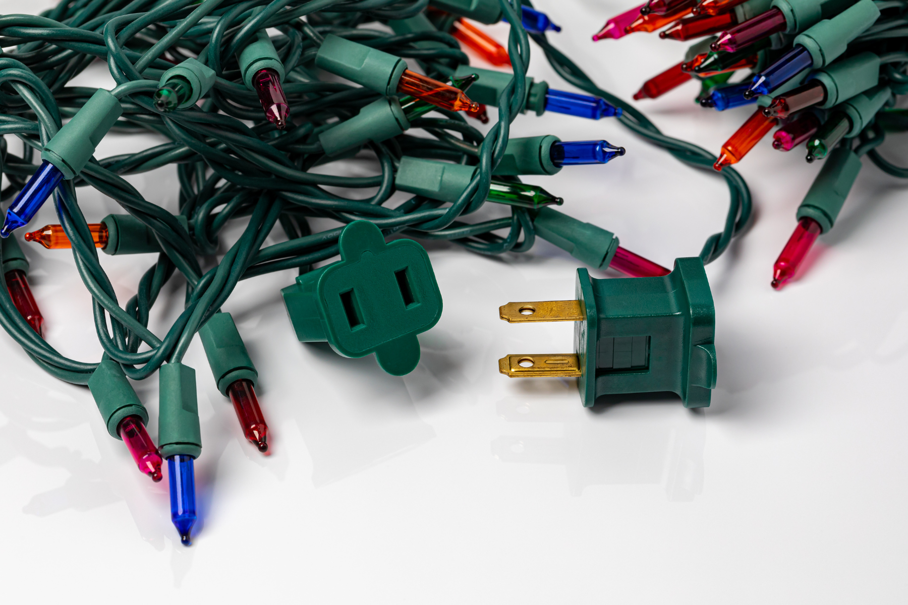 A coiled strand of multicolored Christmas lights lies beside a green power plug and extension connection.