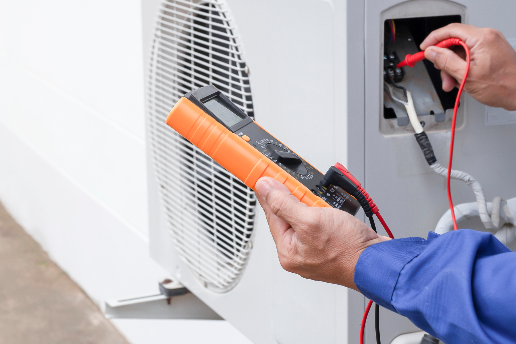A technician uses a multimeter to test the electrical components of an outdoor air conditioning unit.