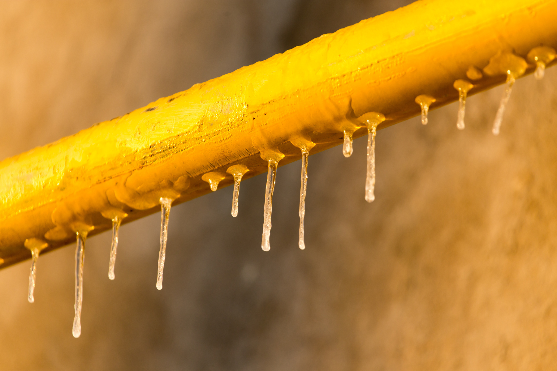A bright yellow outdoor pipe is lined with hanging icicles, indicating extremely cold temperatures and potential freezing issues.