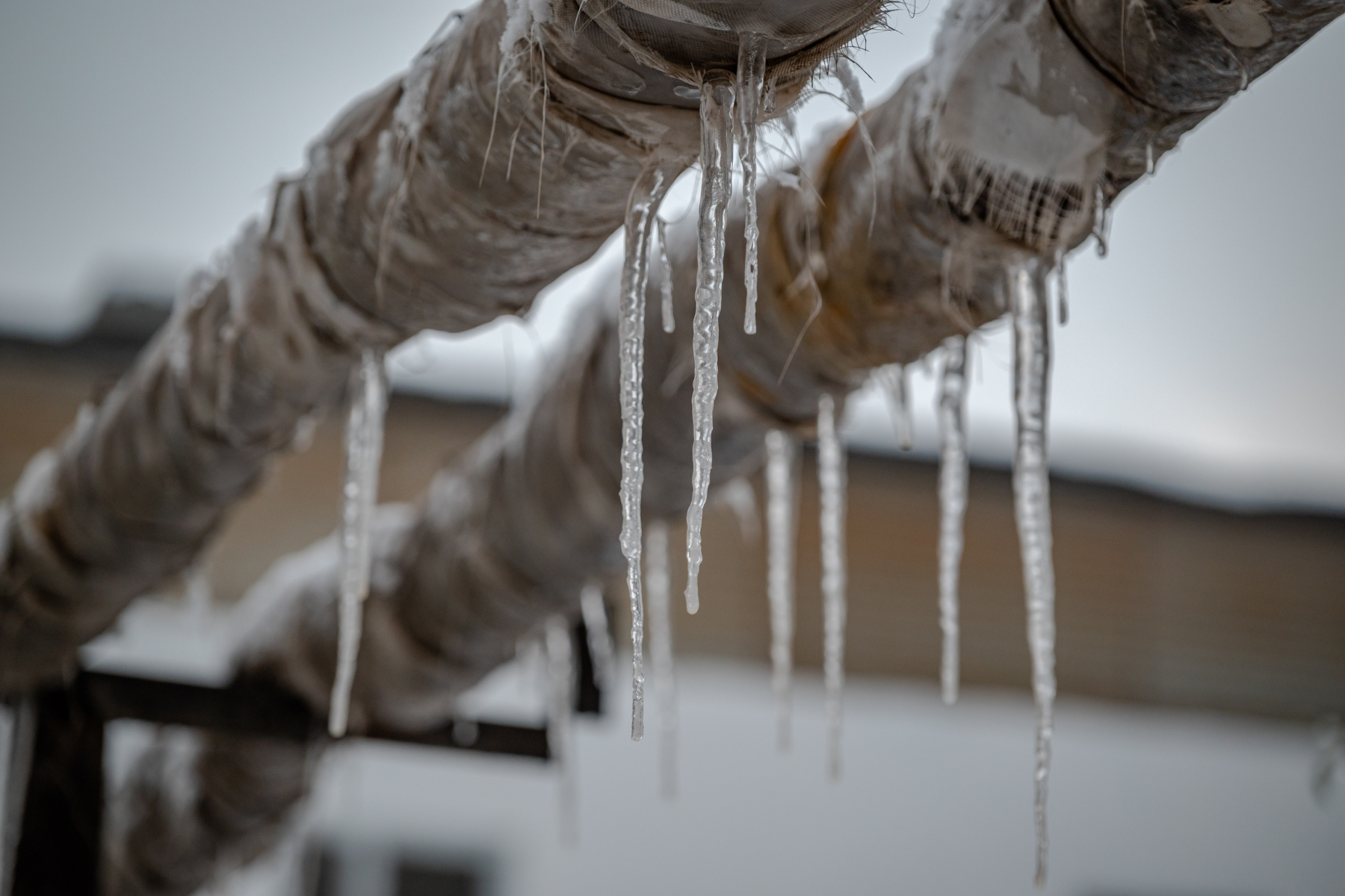 Outdoor insulated pipes are covered in ice and icicles, showing severe freezing that could lead to pipe damage.