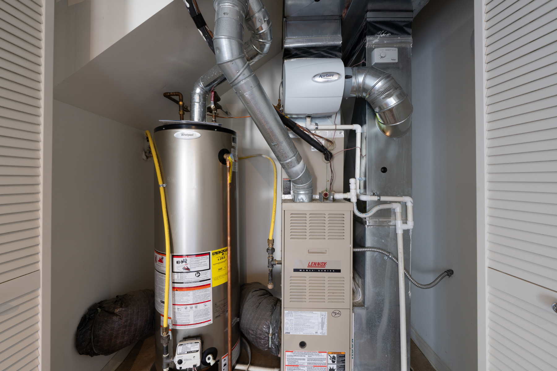 A residential HVAC setup with a gas furnace, ductwork, humidifier, and a tall water heater tightly installed inside a utility closet.