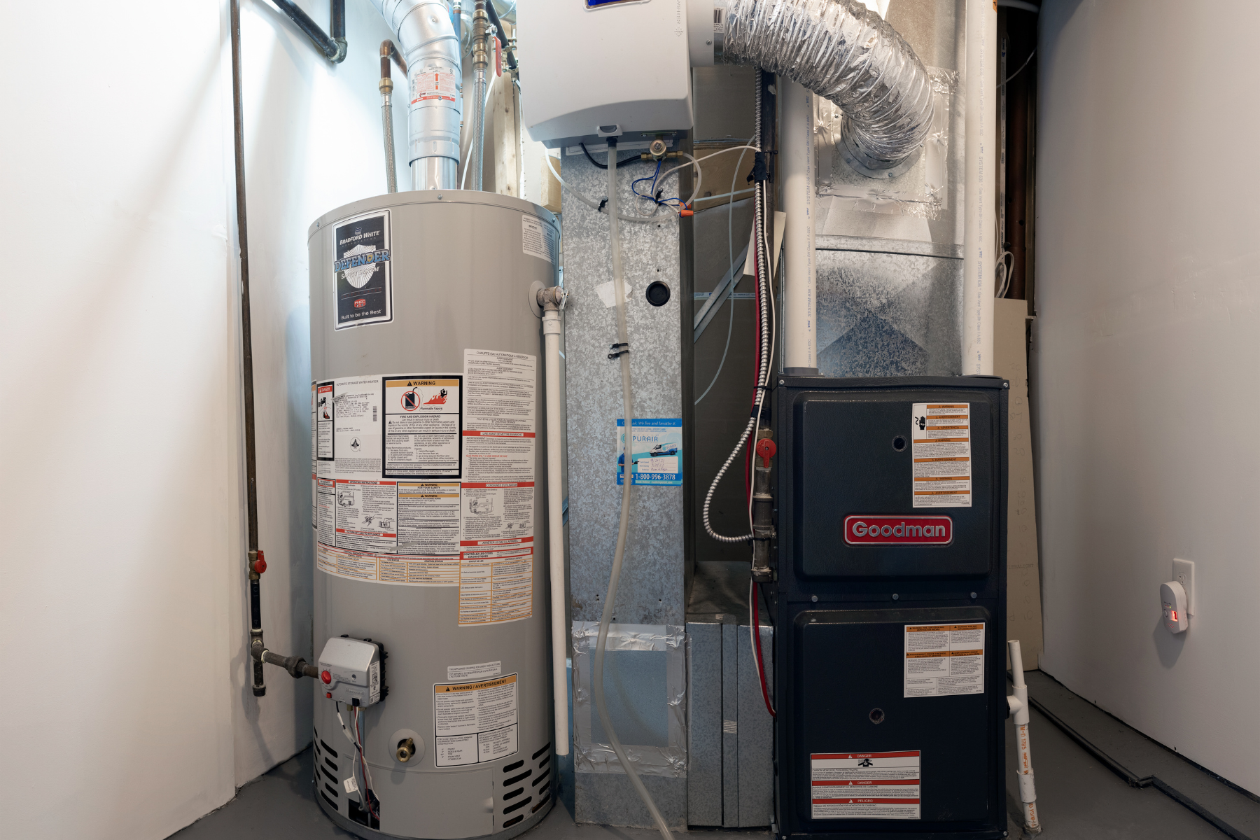 A residential mechanical room with a furnace, ductwork, and a hot water tank installed side by side.