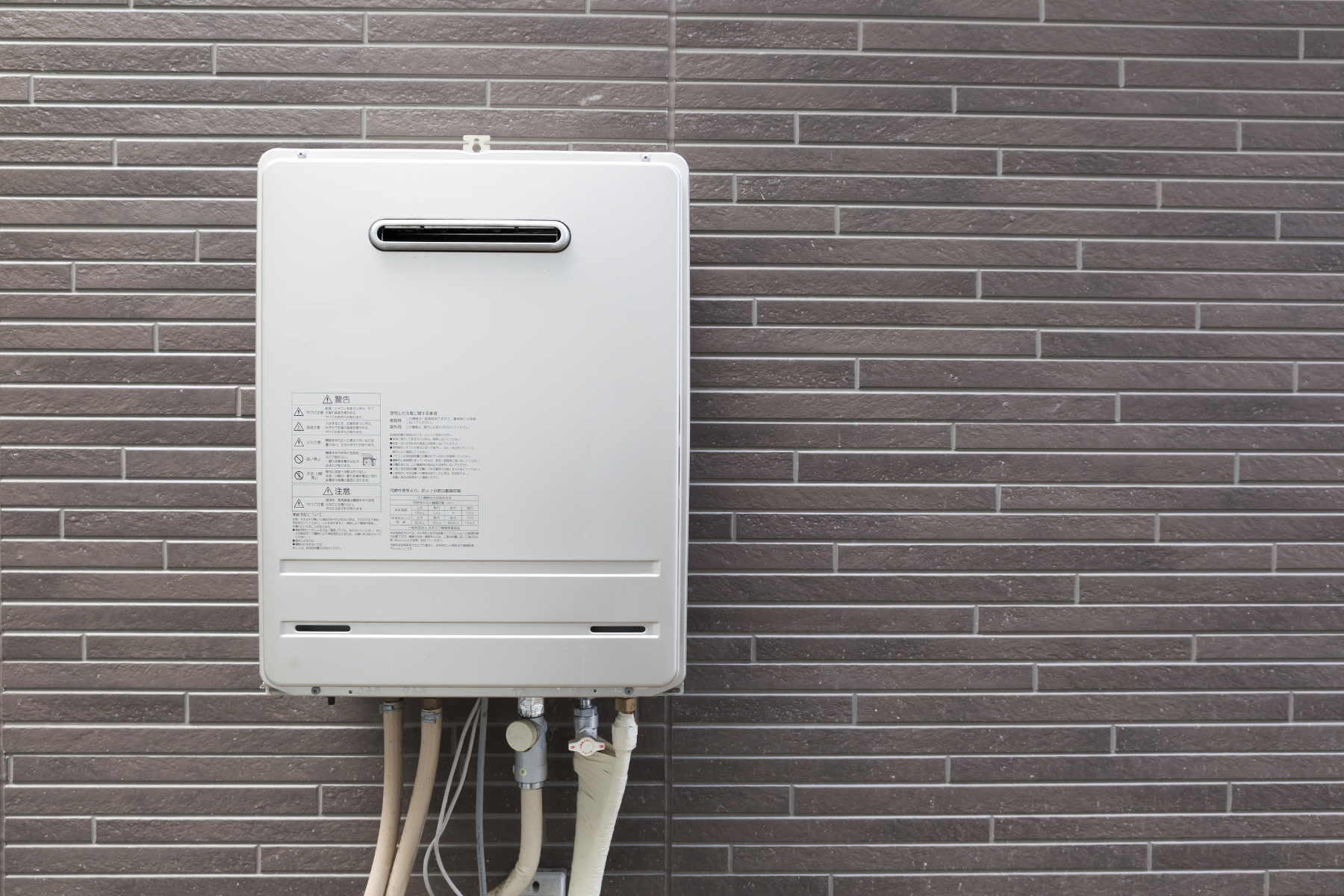 An exterior tankless water heater mounted on a brick wall, used for heating water efficiently.