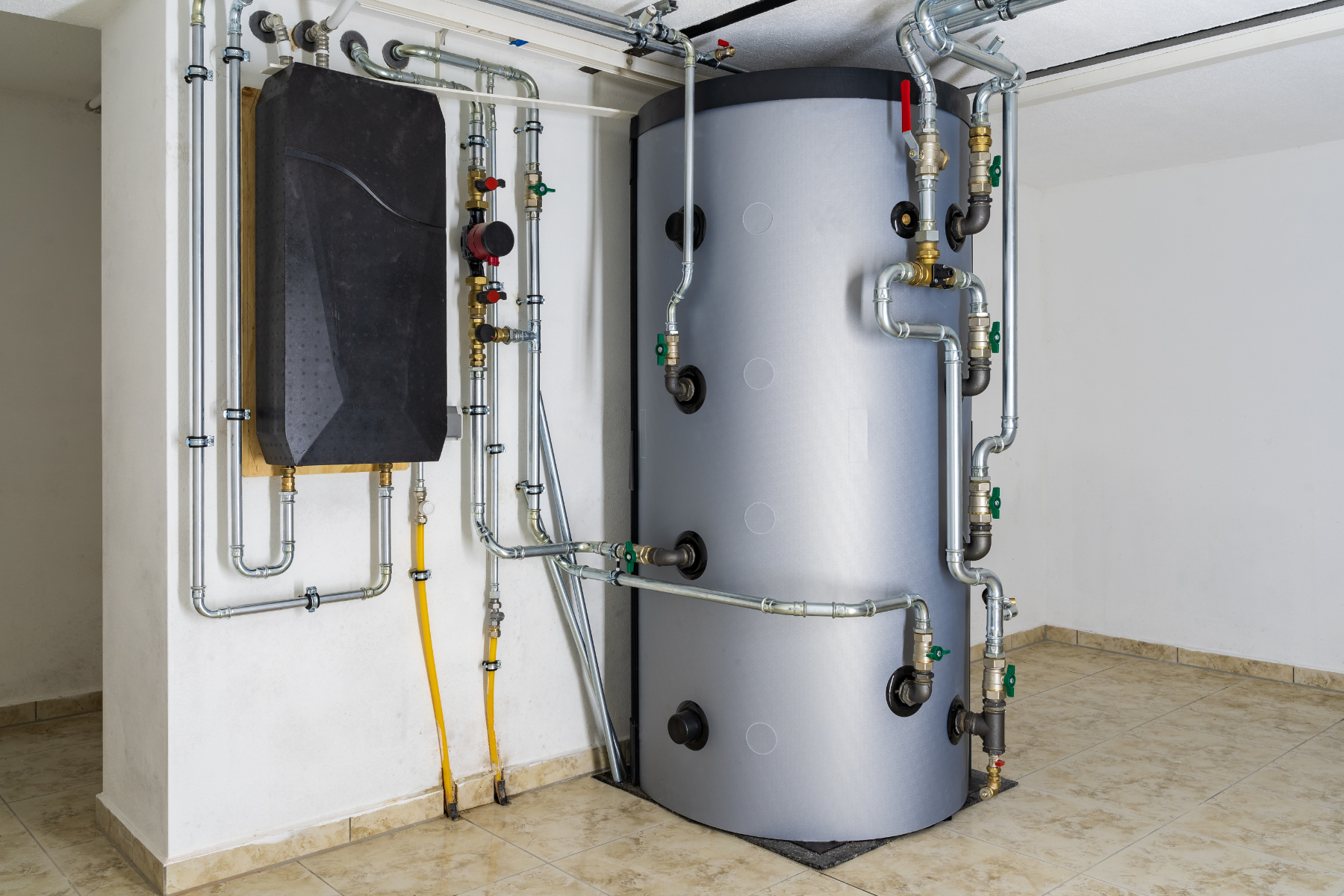 A large, modern residential water heater system installed in a utility room with various connected pipes and valves.