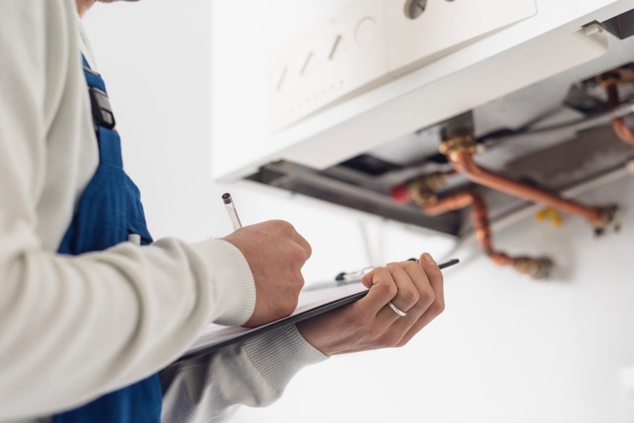 Boiler Check Professional plumber checking a boiler at home and writing on a clipboard