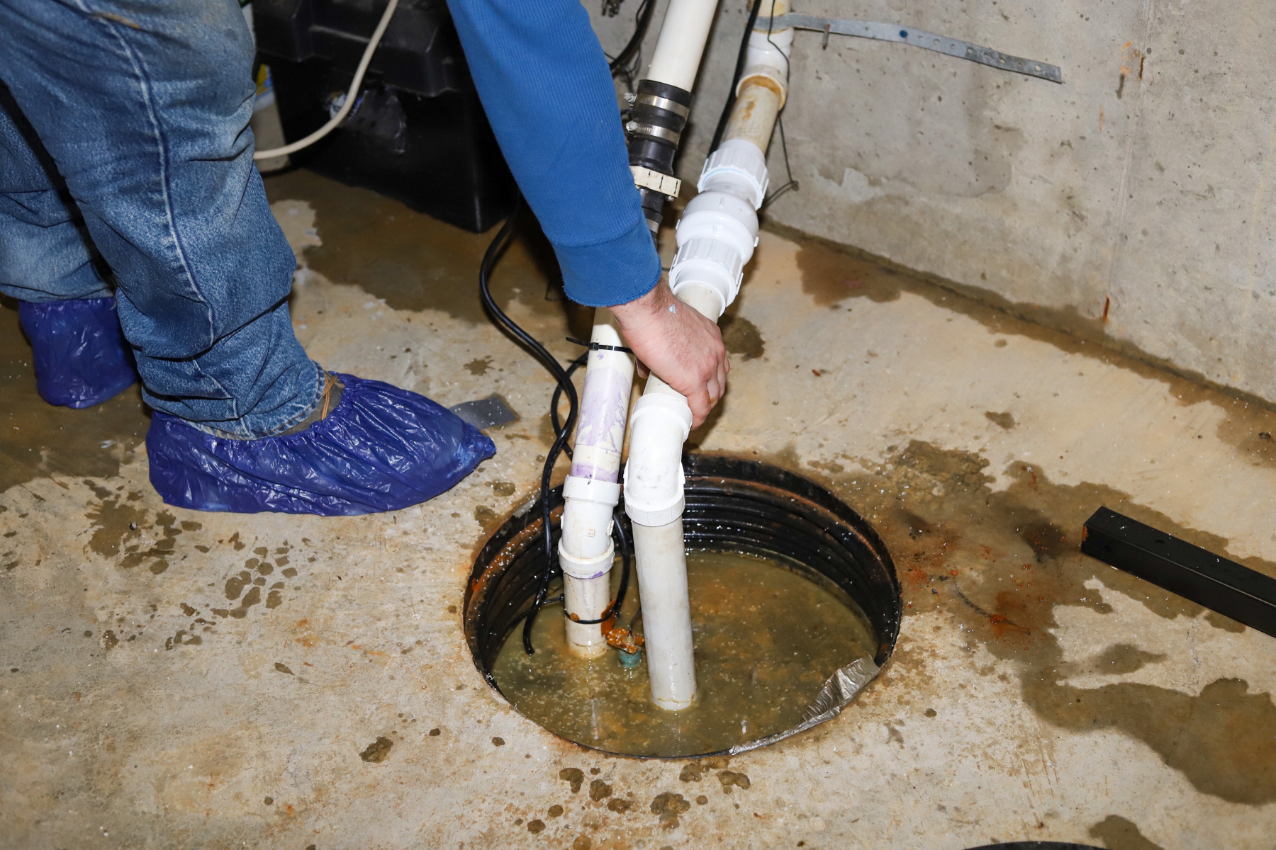 A technician working on a sump pump in a wet basement pit.