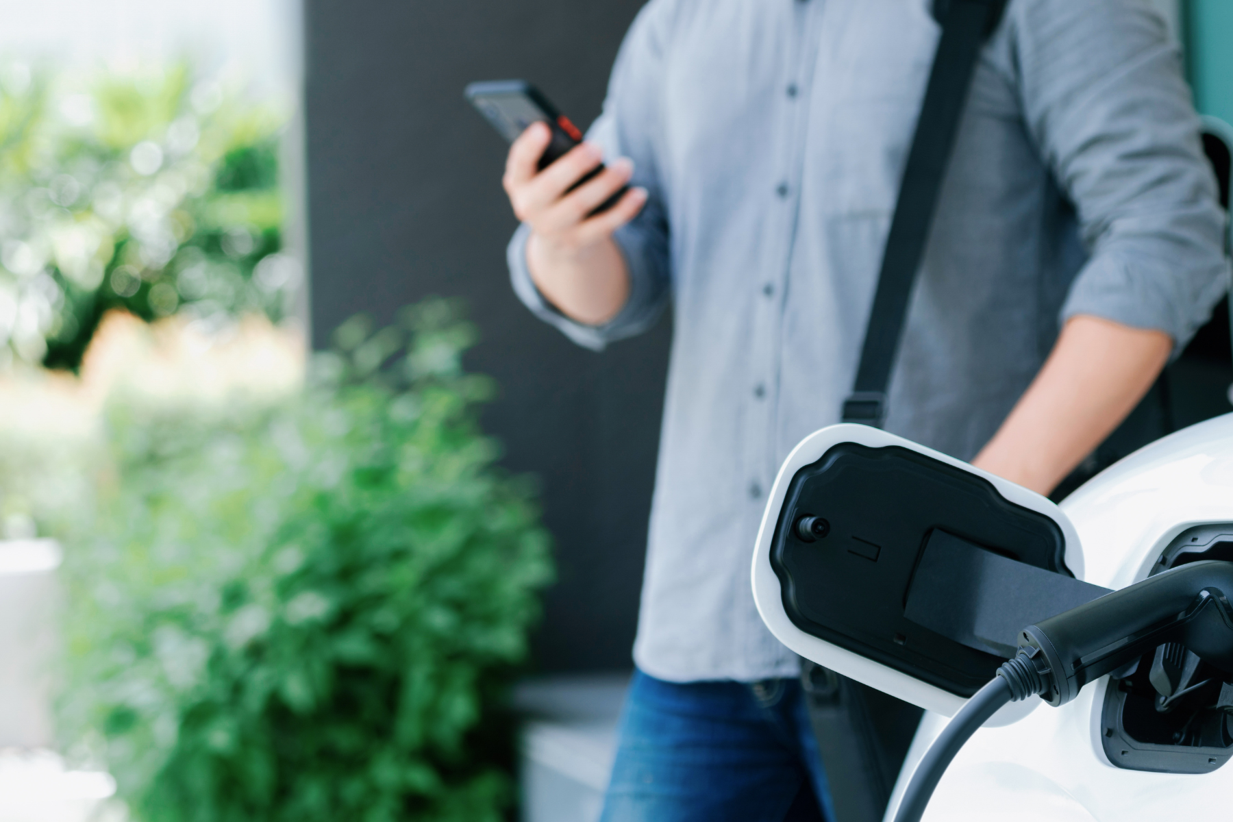 Person standing next to car using phone while car is charging.