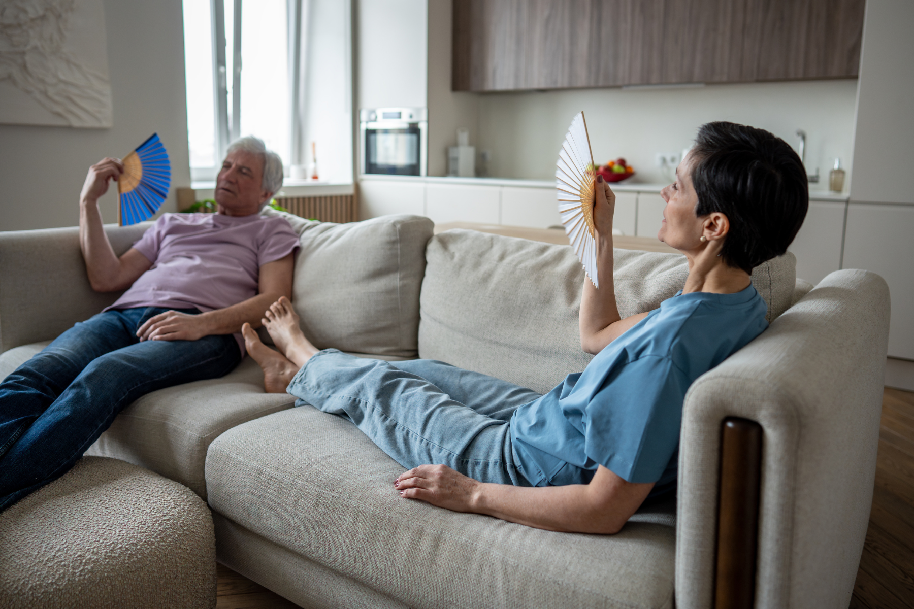 People sittig on couch with fan because its hot.