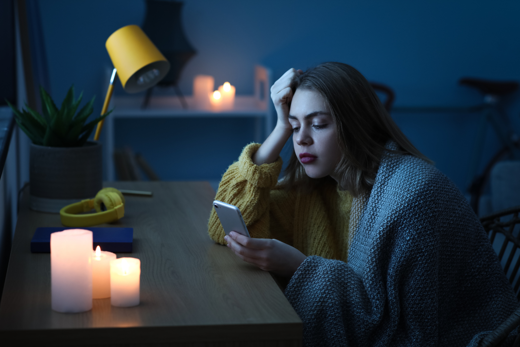 Womans leaning on desk while she uses her phone. Candles are light up while there is a power outage