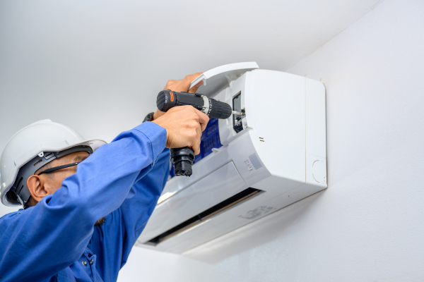 Electrician opening up AC indoor unit by removing screws with drill.